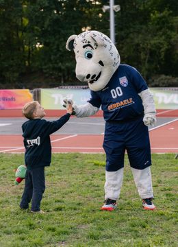 Kind geeft Kids4Kids Sportfestival mascotte een high-five